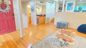 A spacious living area with a wooden floor, a red door, and a kitchen in the background. - Spacious House with heated 24ft swim spa pool (Tampa)