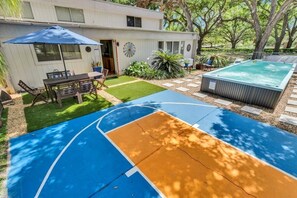 A backyard with a basketball court, a hot tub, and a patio area with outdoor furniture.