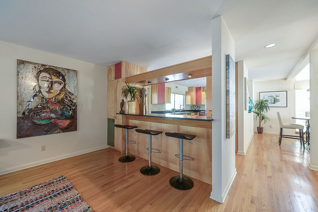 Une cuisine moderne avec un îlot central en bois, trois tabourets de bar et un grand tableau abstrait accroché au mur.