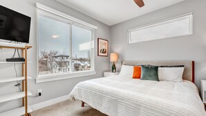 Une chambre avec une grande fenêtre, un lit avec une literie blanche, une table de chevet avec une lampe et un téléviseur posé sur un meuble.