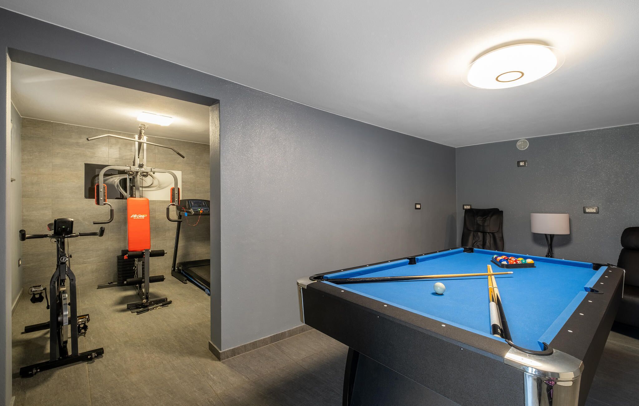 Une pièce équipée d’une table de billard, d’appareils de musculation et d’un espace détente avec des sièges.