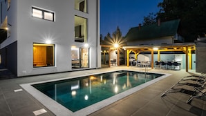 A modern two-story house with a swimming pool, outdoor seating, and a barbecue area.