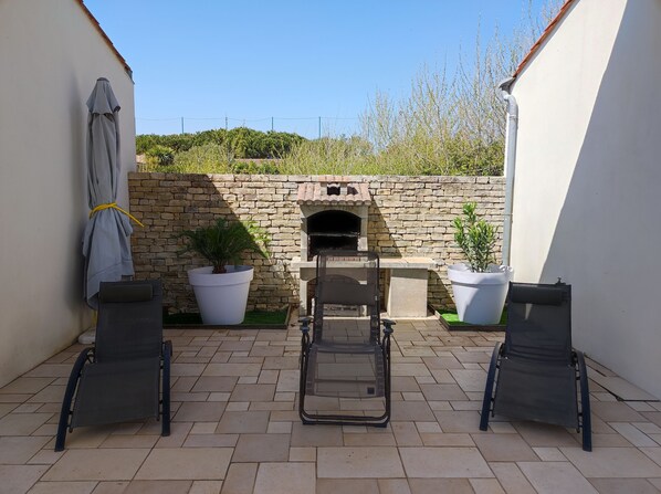 Un patio con dos sillas, un muro de piedra, un horno de ladrillo y plantas en macetas.