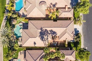 A large, multi-story building with a tiled roof, multiple swimming pools, and palm trees.