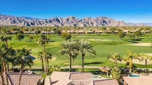 A golf course with a mountain backdrop, palm trees, and resort buildings. - PGA West, private pool and spa outdoor covered TV (La Quinta)