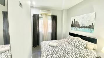 A hotel room with a bed, a nightstand, a painting on the wall, and a window with curtains.