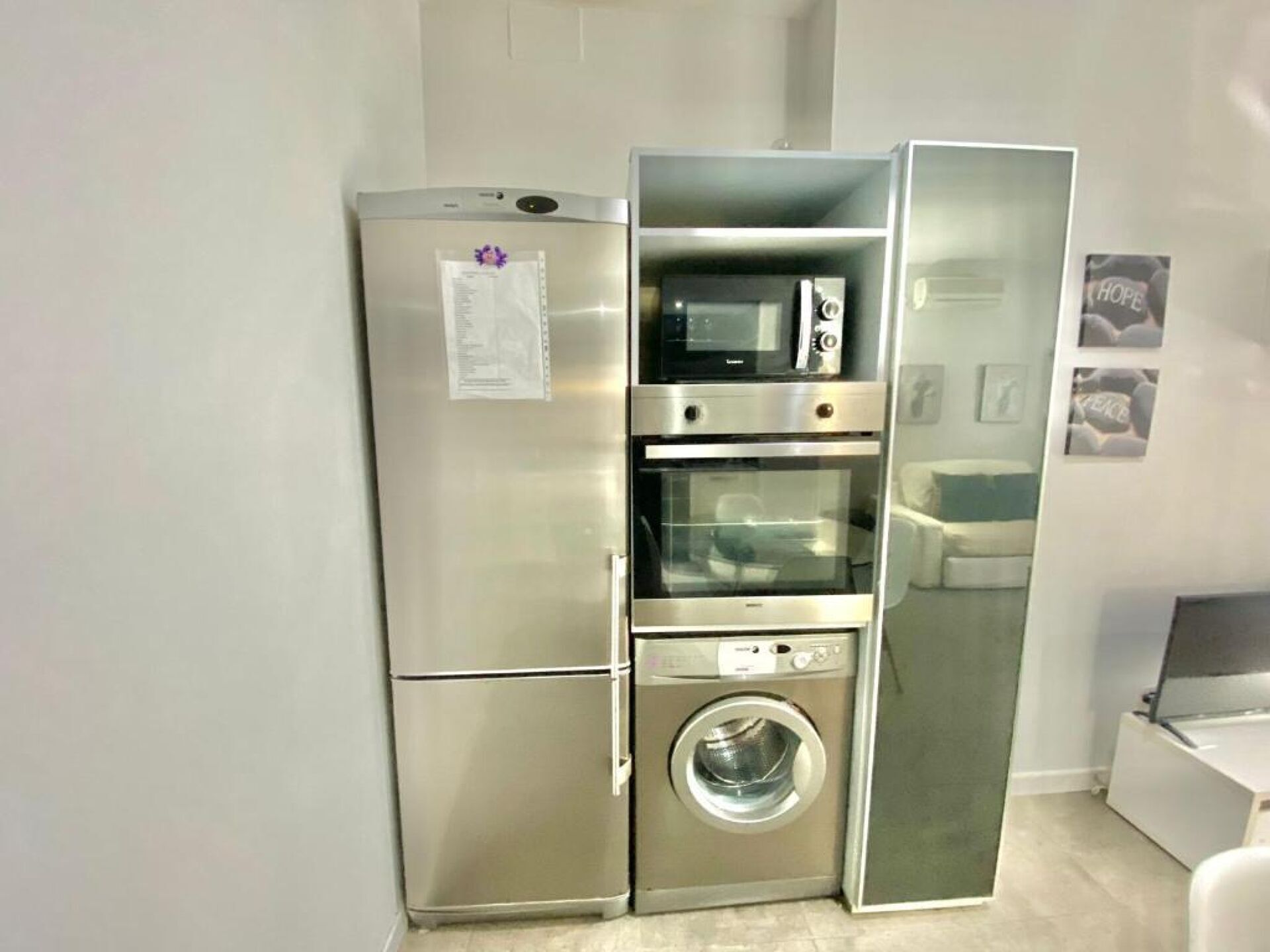 A compact kitchen with a built-in refrigerator, microwave, oven, and washing machine.