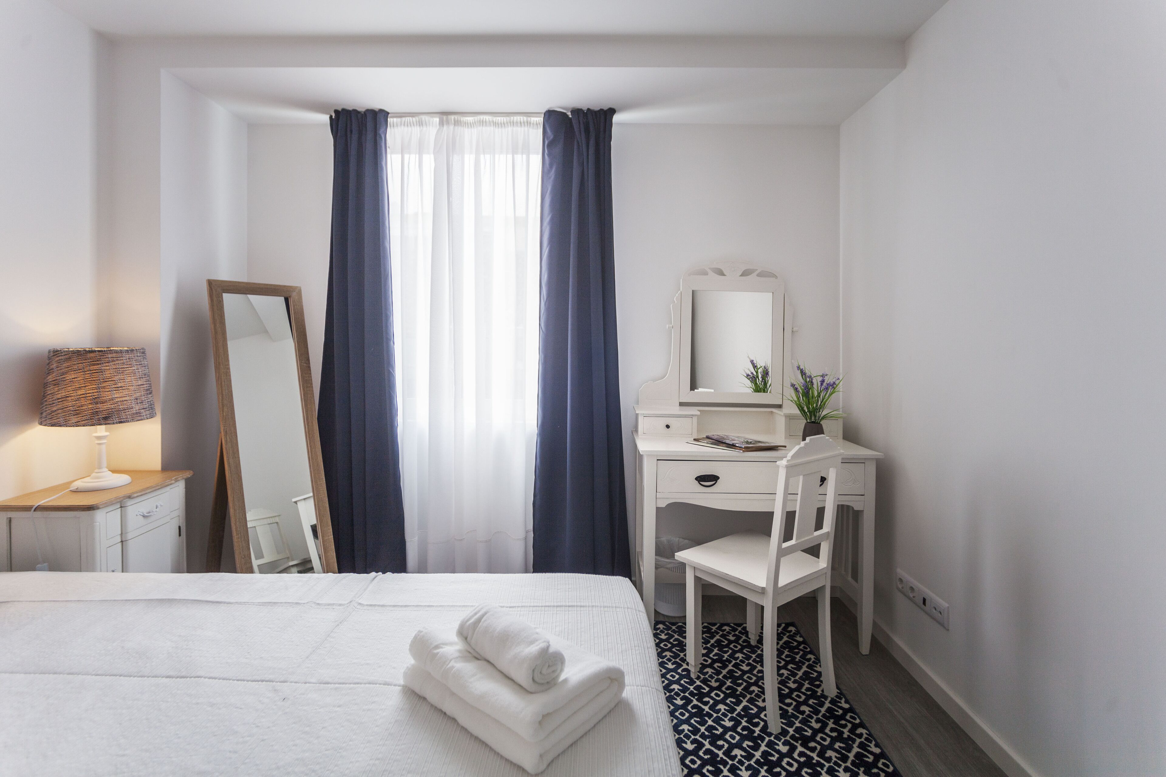 Quarto de hotel com cama, escrivaninha, cadeira, espelho e janela com cortinas.