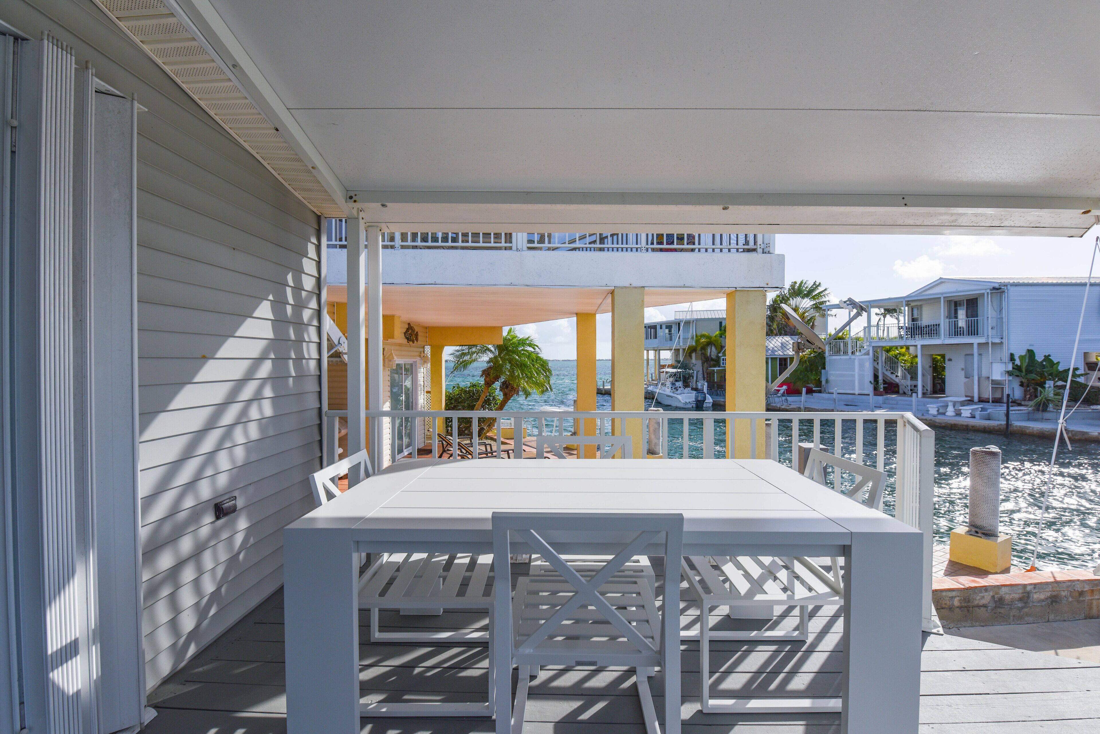 A covered outdoor area with a table and chairs, overlooking a marina with boats and buildings.
