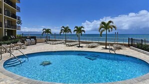 A swimming pool with lounge chairs and palm trees, overlooking a beach.