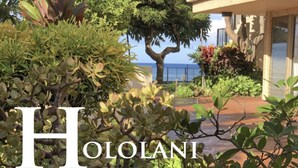 A hotel with a view of the ocean, surrounded by lush greenery and a well-maintained garden.