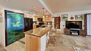 A modern kitchen with a central island, built-in appliances, and a dining area with a TV and seating.