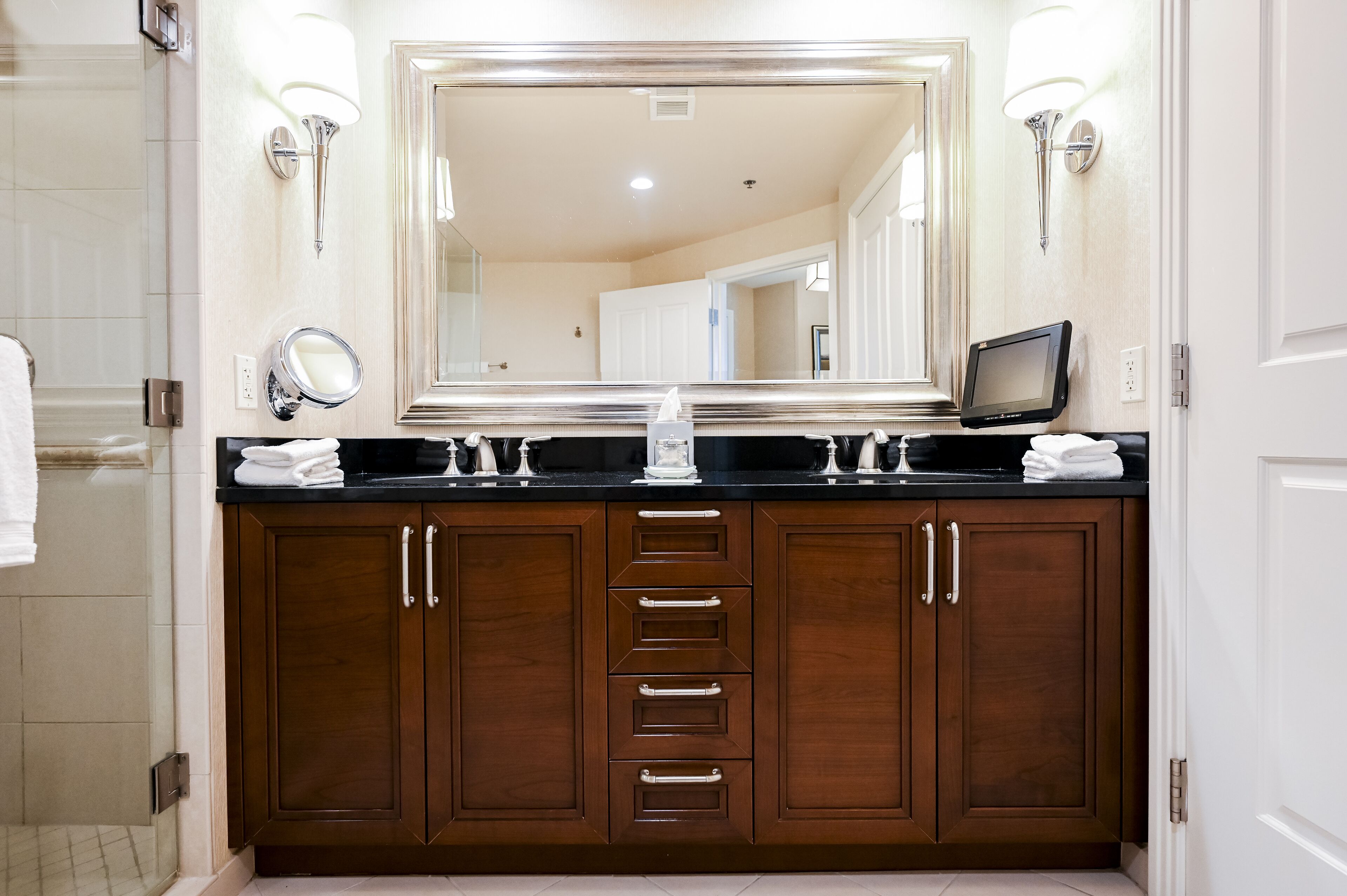 A bathroom with a large mirror, wooden cabinets, a black countertop, and two wall-mounted lights.