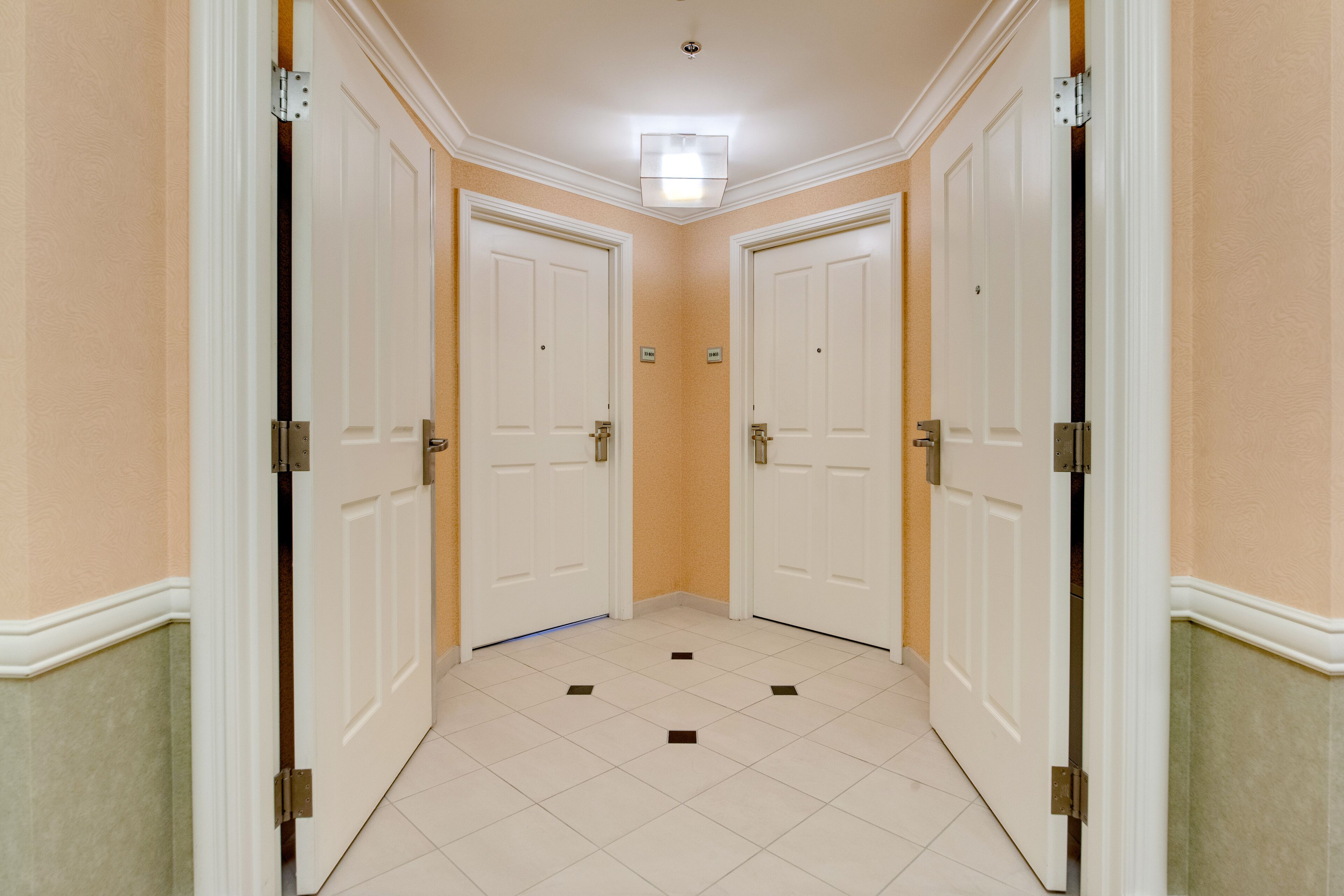 Un couloir avec deux portes blanches, des murs de couleur beige et un sol carrelé.