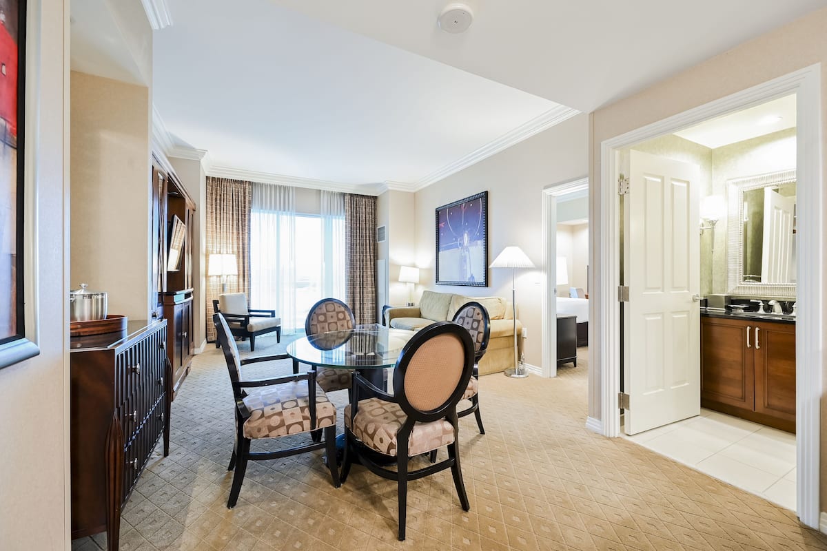 A hotel room with a dining area, a sofa, a TV, and a kitchen.