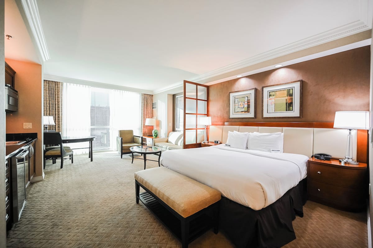A hotel room with a large bed, a desk, a chair, a bench, a nightstand, and a TV.