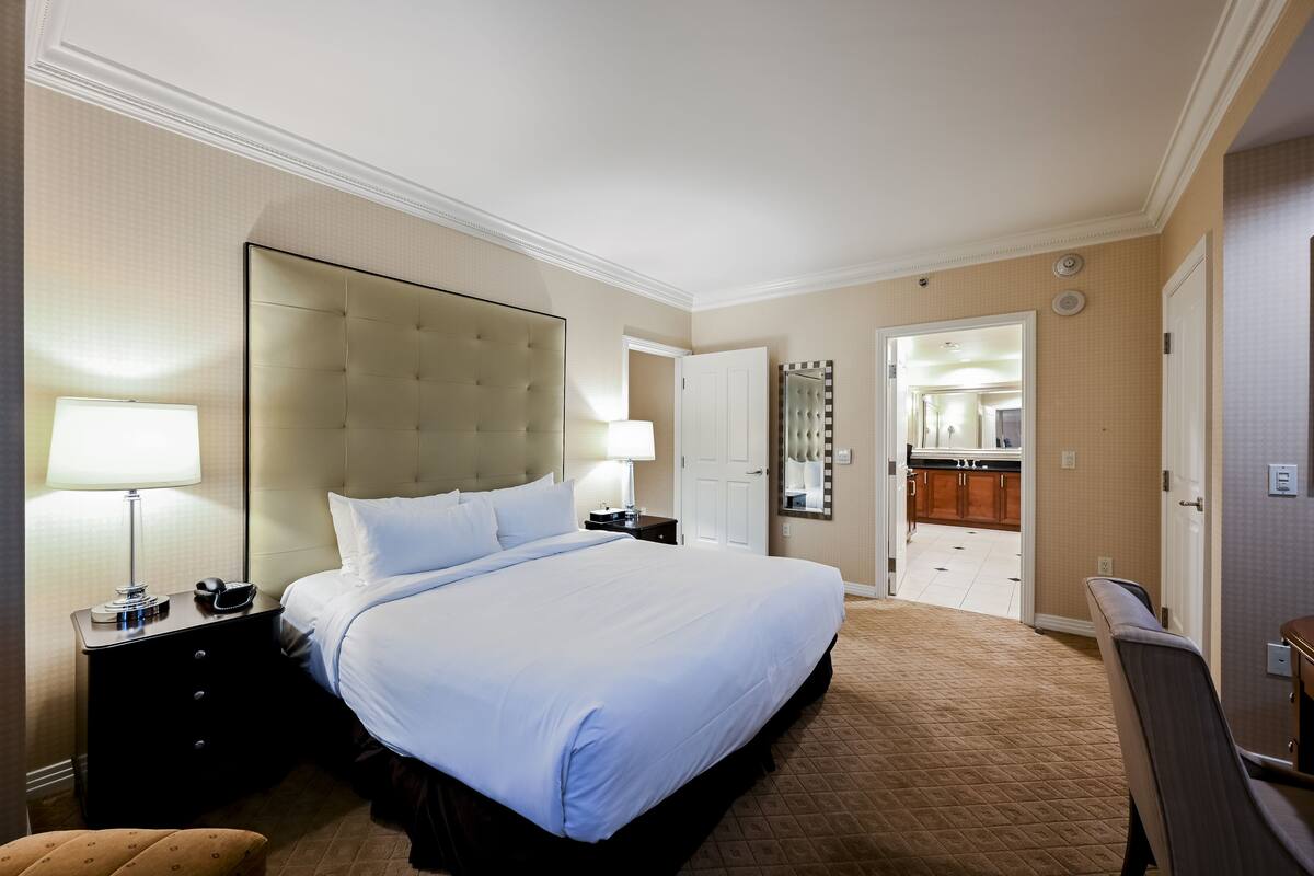 A hotel room with a large bed, a nightstand with a lamp, a dresser, and a mirror.