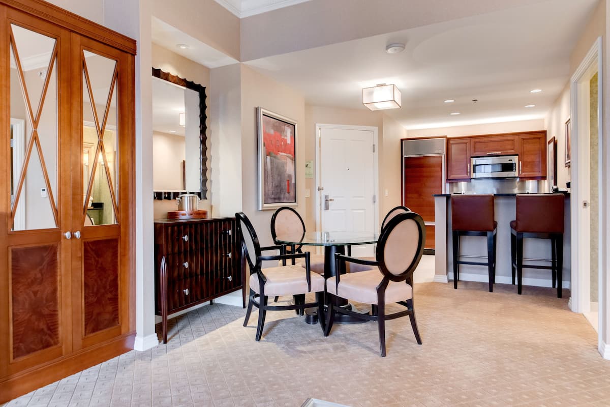 A dining area with a round table and chairs, a kitchen with a microwave and cabinets, and a wooden cabinet with glass doors.