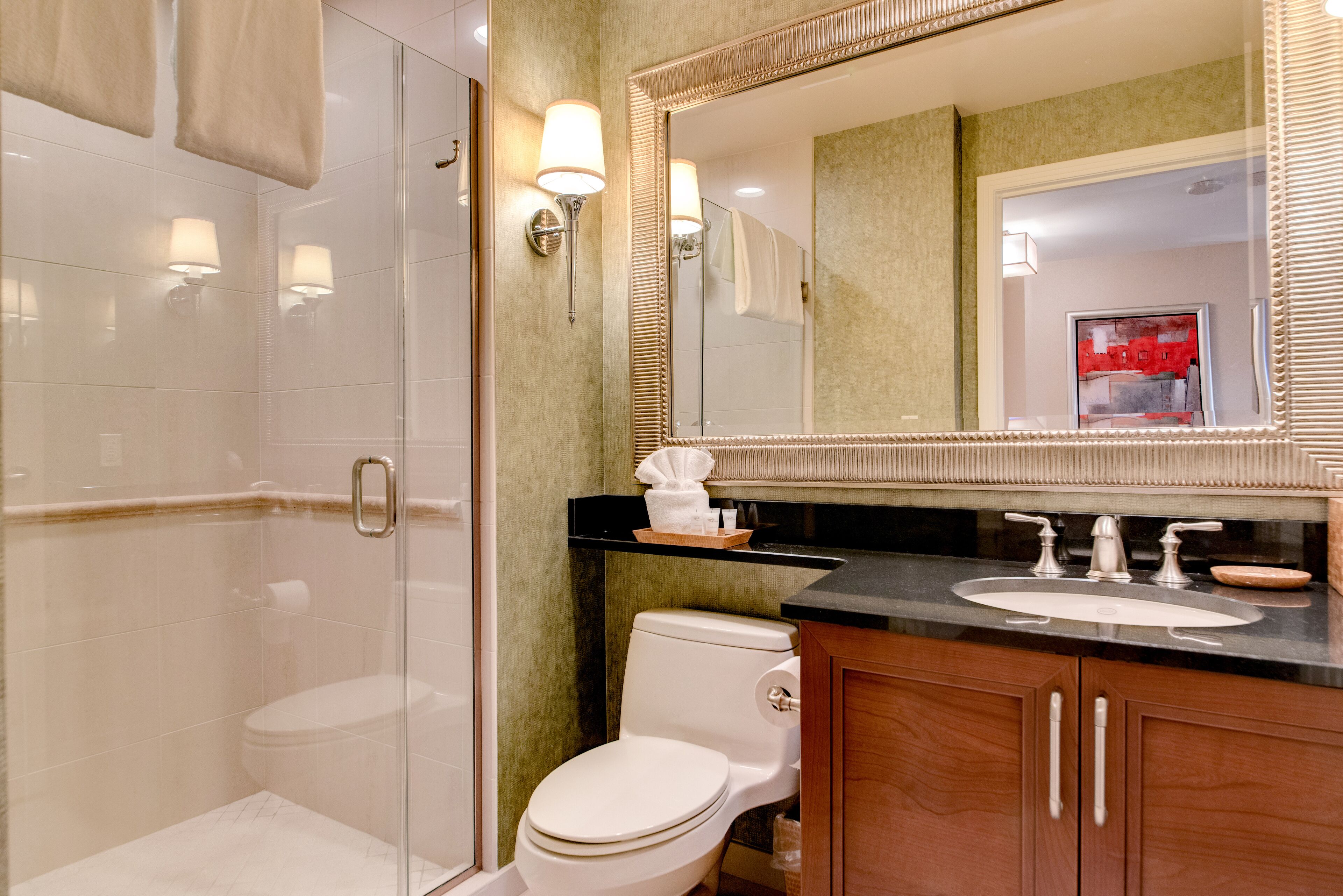 A modern bathroom with a glass shower enclosure, a white toilet, and a vanity with a large mirror and sink.