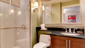 A modern bathroom with a glass shower enclosure, a white toilet, and a vanity with a large mirror and sink.