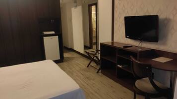 A hotel room with a bed, a desk with a chair, a television, and a small refrigerator.