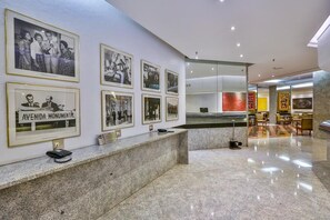 A lobby with a reception desk, framed photographs on the wall, and a seating area with chairs. - Flat Plaza Hotel - Setor de Hotéis Norte (Brasília)