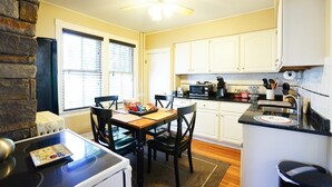 A compact kitchen with white cabinets, a black countertop, and a dining area with a table and chairs. - Atlantic Street Guesthouse - The Best Kept Secret! (Newport)