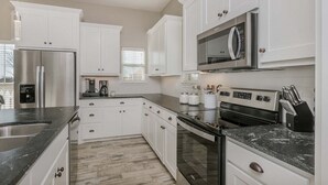 Cocina moderna con armarios blancos, electrodomésticos de acero inoxidable y encimera de granito.