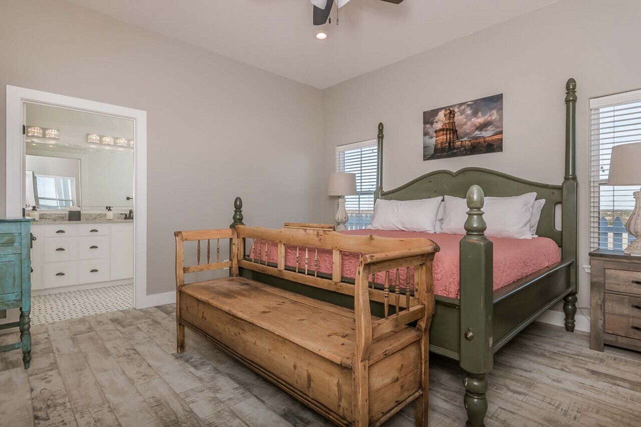 Quarto com um banco de madeira, uma cama de dossel verde, um espelho e uma pintura na parede.