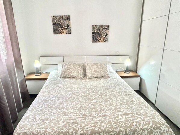 A bed with a patterned bedspread, two bedside lamps, and two wall-mounted artworks.