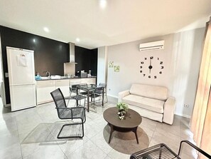 A modern living room with a sofa, a coffee table, and a dining area with chairs and a table.