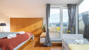 A hotel room with two beds, a wooden wardrobe, a balcony with a view, and a small table with a vase of flowers. - HostWise - Seaside Beach Flat (Vila Nova de Gaia)