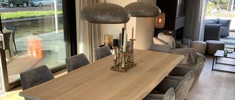 A modern dining area with a wooden table, grey upholstered chairs, and hanging pendant lights.