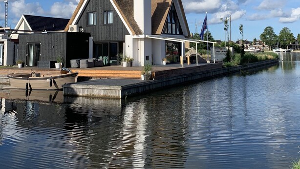 Ein modernes Haus mit einem großen Erkerfenster, einer überdachten Terrasse und einem Steg mit einem Boot.