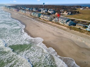 An aerial view of a coastal residential area with beachfront properties, a pier, and a water tower.