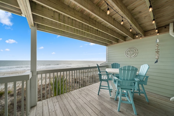 A wooden deck with a view of the ocean, a table with chairs, and a compass on the wall.