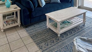 Un soggiorno con un divano blu scuro, un tavolino da caffè bianco e una televisione. Sono presenti due lampade sui tavolini laterali e si vede una ventola a soffitto.