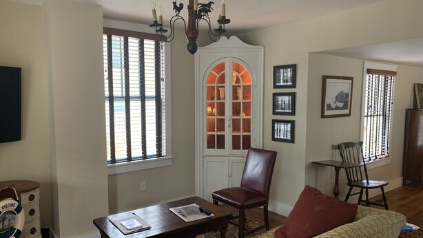 A living room with a sofa, a wooden coffee table, a red chair, a white cabinet with glass doors, and a chandelier.