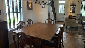 A dining area with a wooden table and chairs, a chandelier, and a staircase leading to another room.