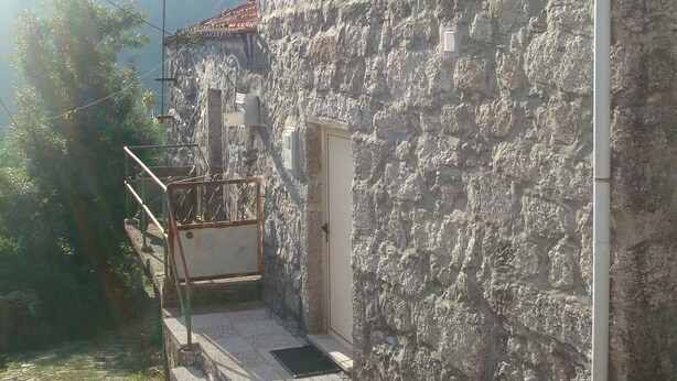 Un edificio de piedra con una puerta pequeña y una ventana, una escalera de metal y un poste de electricidad.