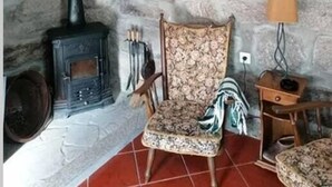 Una habitación rústica con pared de piedra, chimenea, una colección de llaves enmarcadas y un sillón estampado.