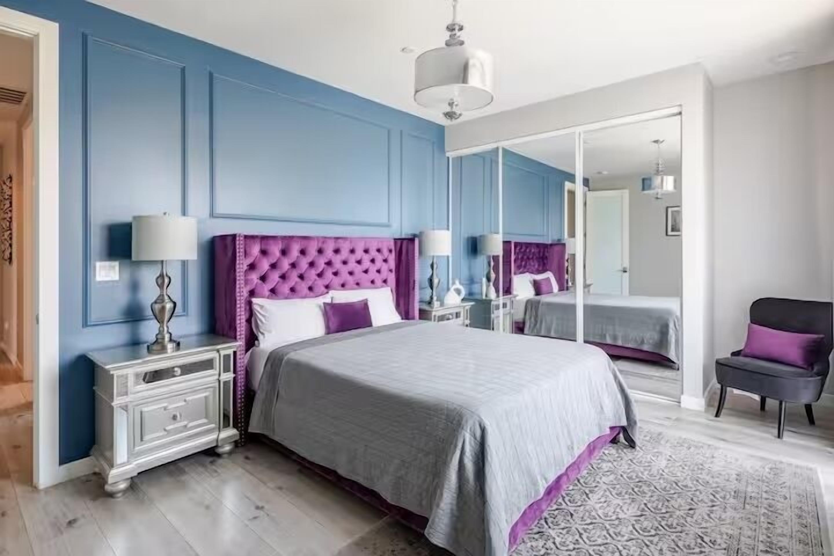 A bedroom with a large bed, a nightstand, a dresser, a chair, and a mirror.