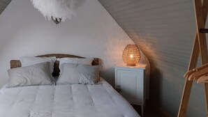 Une chambre avec un plafond haut, un lit avec une literie blanche, une table de chevet avec une lampe et une chaise en bois.