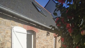 Un bâtiment en pierre avec une porte blanche, des plantes en pot et un chemin pavé de briques.