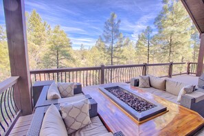Eine Terrassensitzgelegenheit im Freien mit Feuerstelle und Blick auf einen Wald.