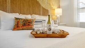 A neatly made bed with a decorative pillow, a tray with a bottle and glasses, and a lamp on a bedside table. - Sailfish Gulf Suites #1, Beachfront, Steps to the Sand (Holmes Beach)