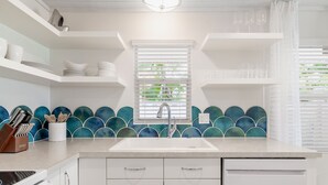 A modern kitchen with white cabinetry, a central sink, and a backsplash with blue and green tiles. - Sailfish Gulf Suites #1, Beachfront, Steps to the Sand (Holmes Beach)
