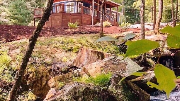 Una cabaña de madera rodeada de árboles y un pequeño arroyo.