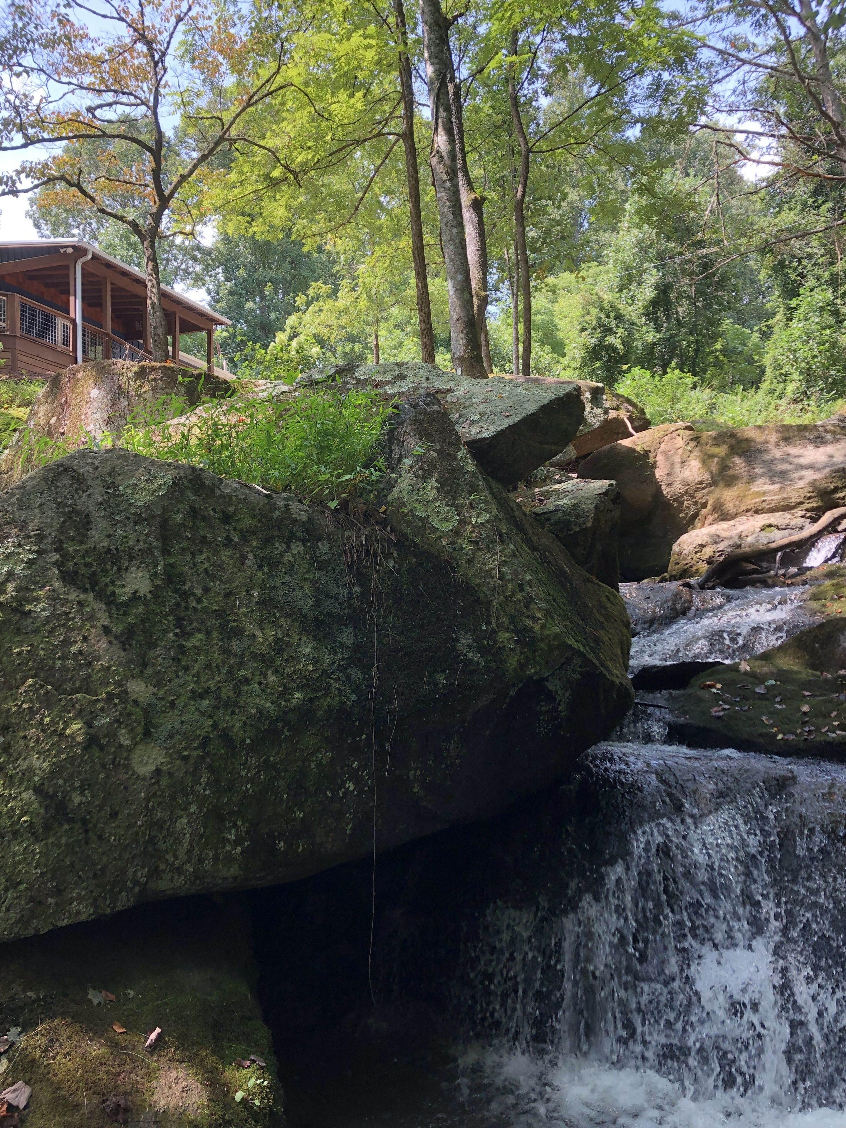 A wooden cabin with a porch overlooking a small waterfall.
