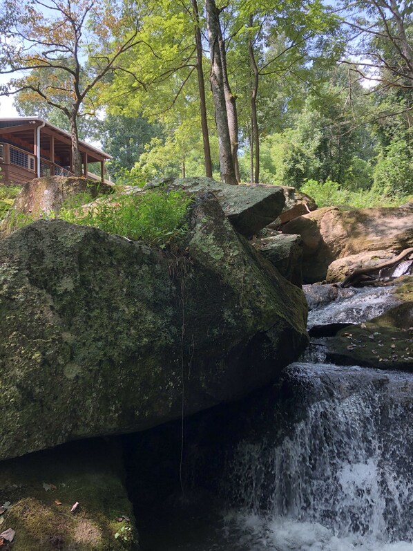 A wooden cabin with a porch overlooking a small waterfall.